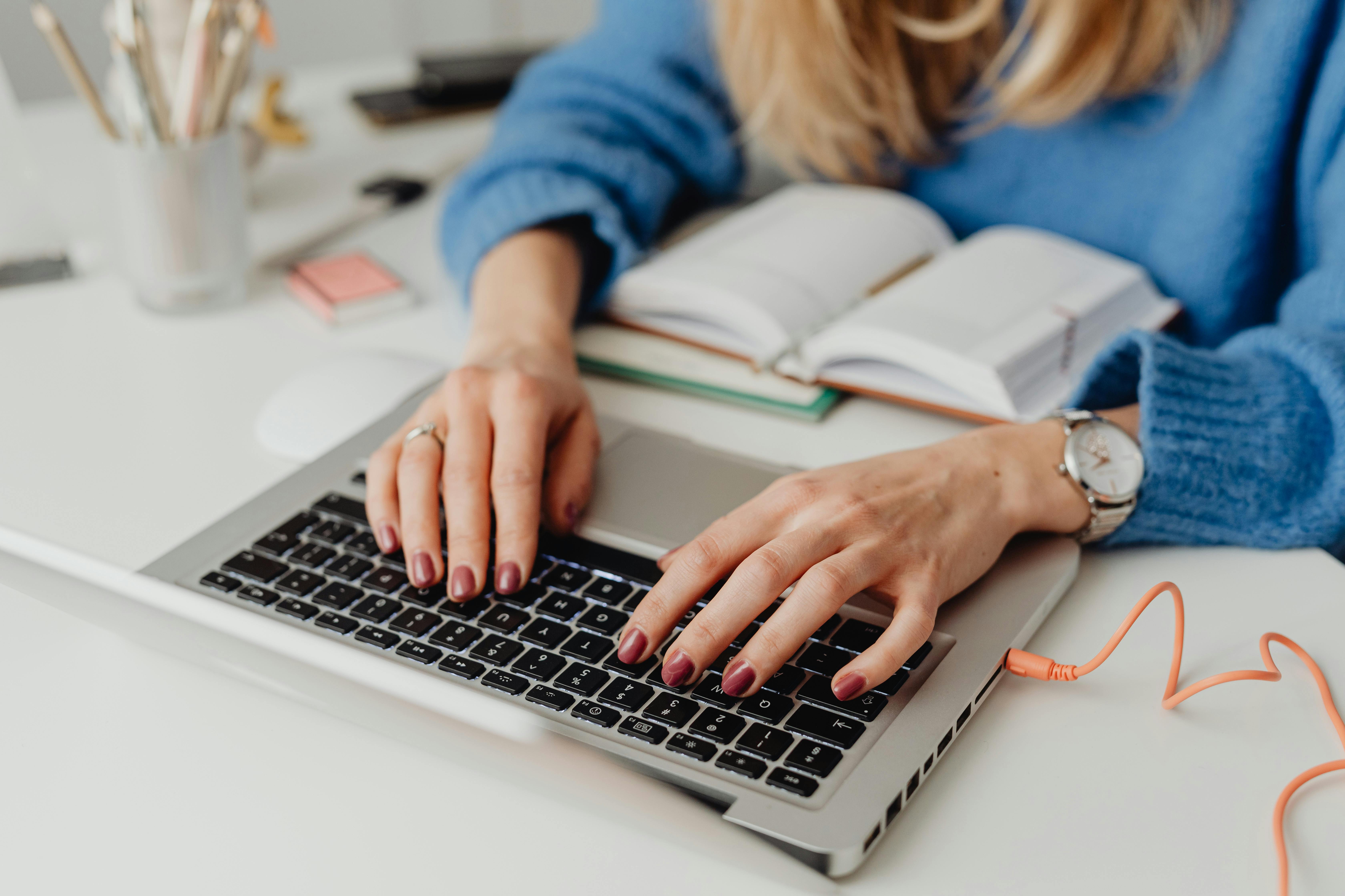 Professional working on a laptop with an open notebook on the desk